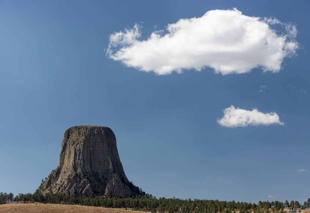 Minimalist view of Devil's tower with 2 clouds in a blue sky