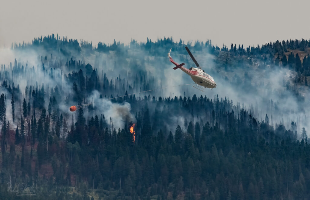 helicopter fighting fire with a Bambi bucket trailing behind as he speeds to the fire