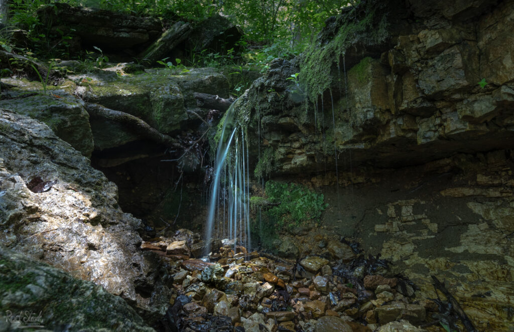 Tiny waterfall trickling over the rocks with dappled lighting